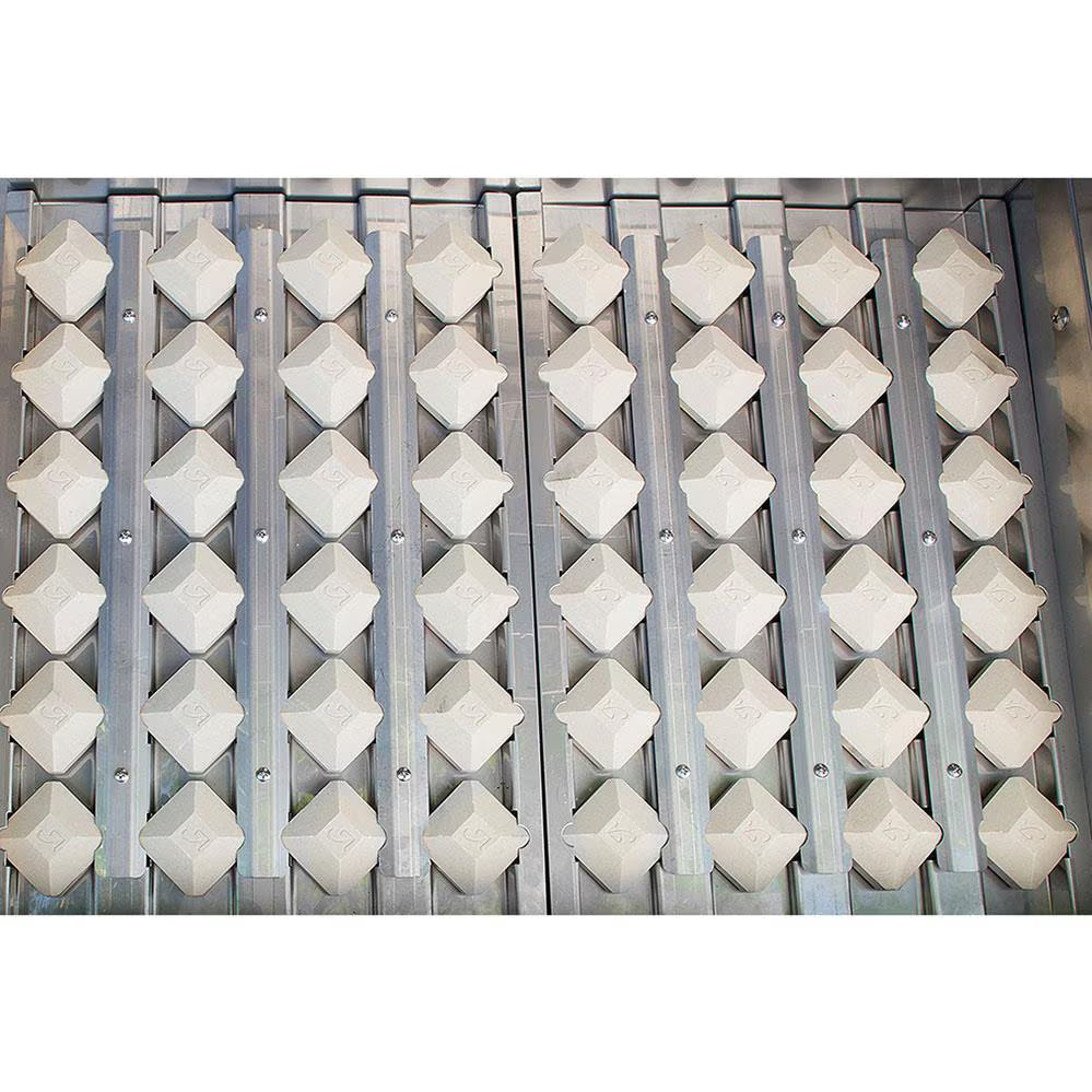 Close-up of rows of white ceramic briquettes beneath the cooking grates inside an Alfresco built-in gas grill, on white background