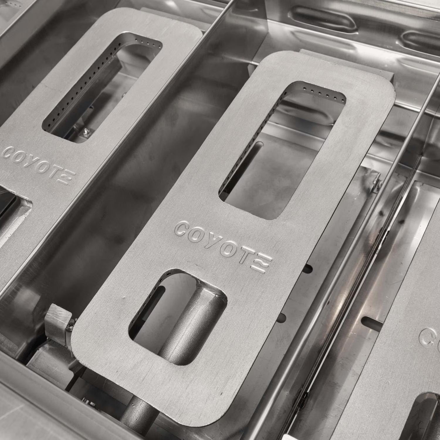 Close-up of stainless steel Coyote-branded heat tents and flame tamers inside a grill firebox