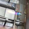 Close-up of a stainless steel grill burner igniting with a blue flame from the electronic igniter