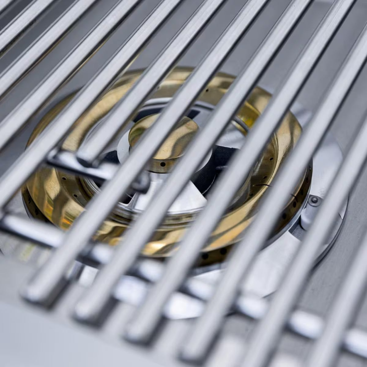 Close-up of a brass gas side burner viewed through stainless steel cooking grates