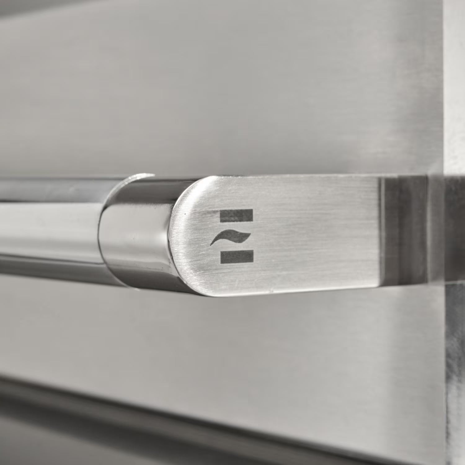 Close-up of the polished stainless steel tubular grill handle end cap with an embossed wave logo, mounted on the brushed steel grill lid