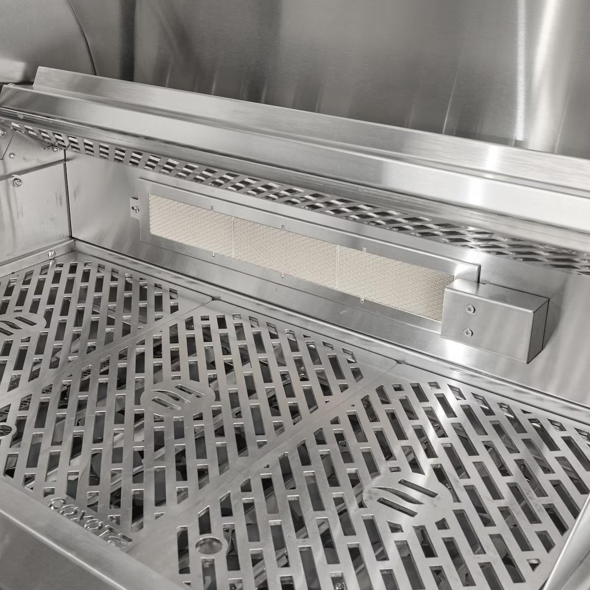 Interior of an open Coyote stainless steel grill showing the rear infrared burner with its mesh screen mounted at the back of the firebox, above the Coyote-branded cooking grates
