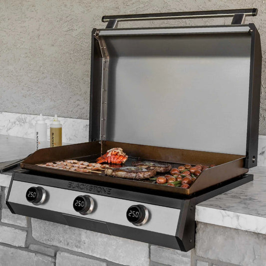 Blackstone 30-inch electric drop-in griddle with open lid cooking shrimp, lobster, and sausage on a marble outdoor counter