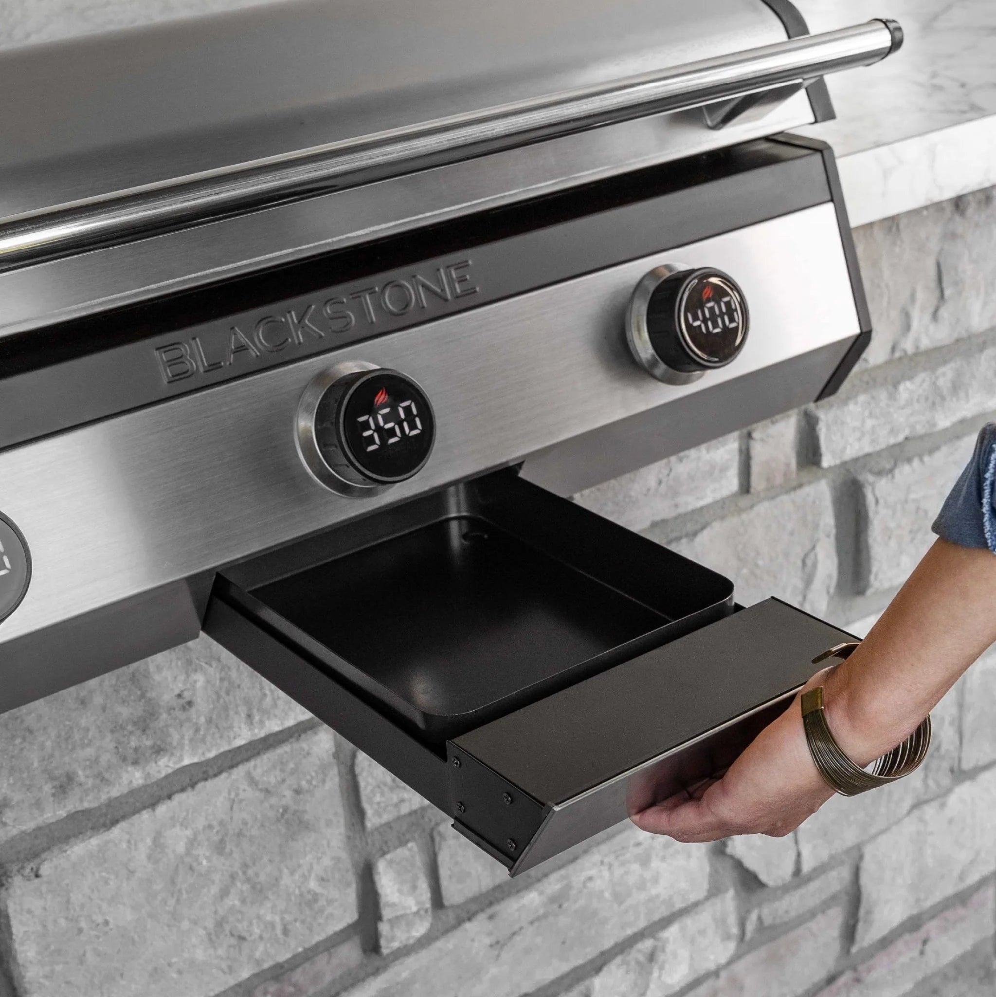 Person pulling out the front-access grease drawer on a Blackstone electric drop-in griddle built into a stone island