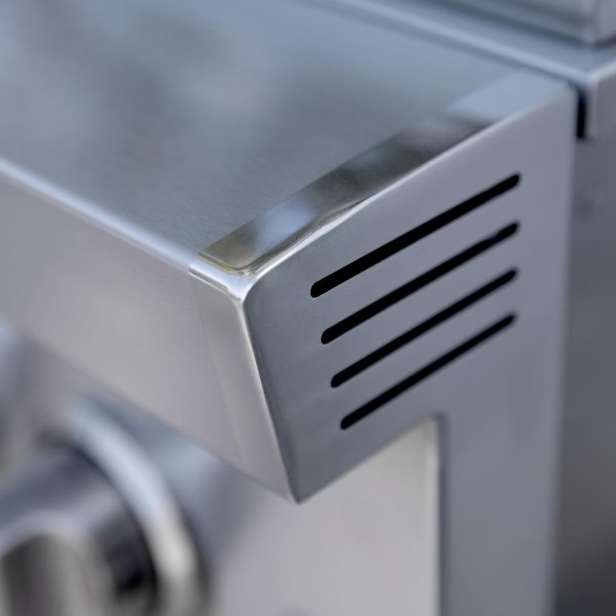 Close-up of a stainless steel grill corner showing ventilation slots and rounded edge detail