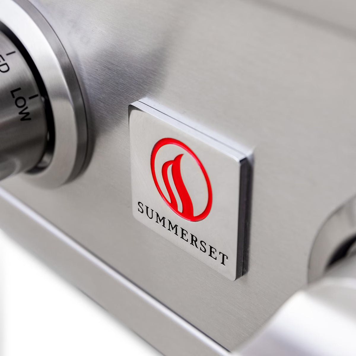 Close-up of the Summerset flame logo badge on the control panel beside a knob of a built-in gas grill