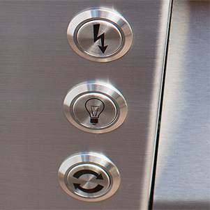 Close-up of three stainless steel ignition, light and rotisserie control buttons on an Alfresco built-in gas grill