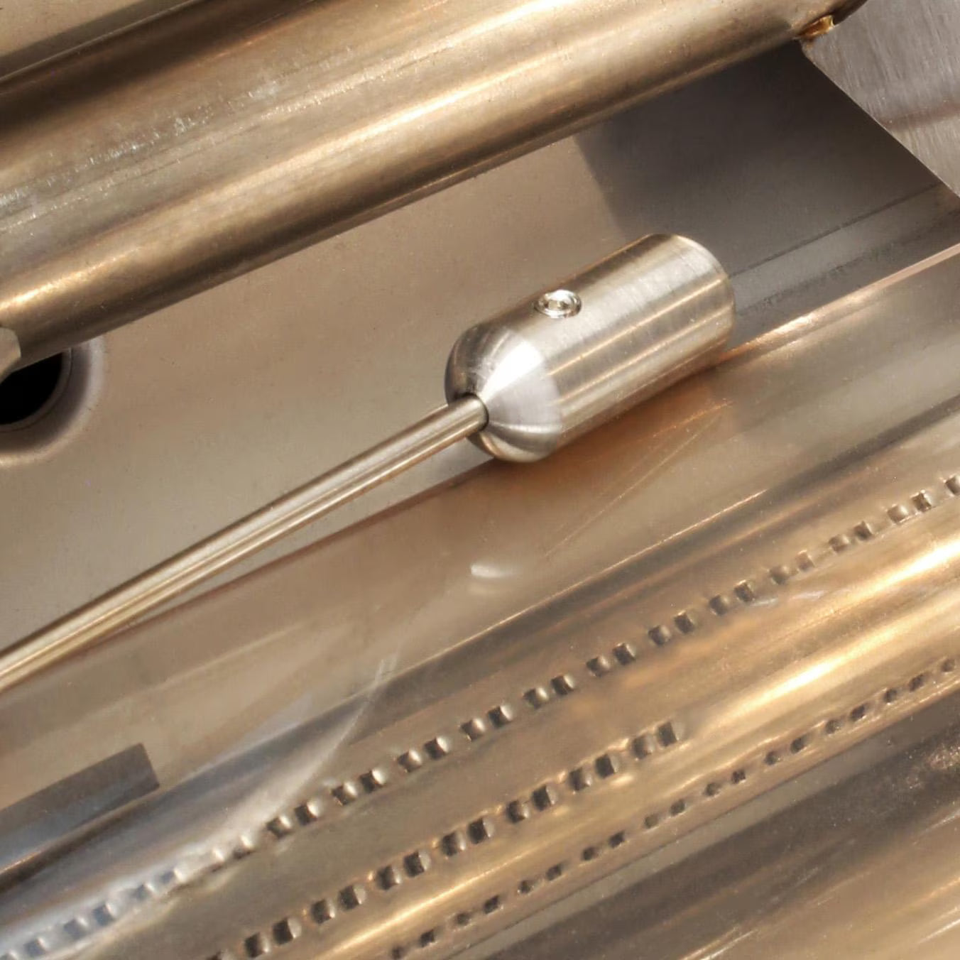 Close-up inside a stainless steel grill firebox showing the cylindrical ignition electrode module mounted at the end of a perforated stainless steel tube burner