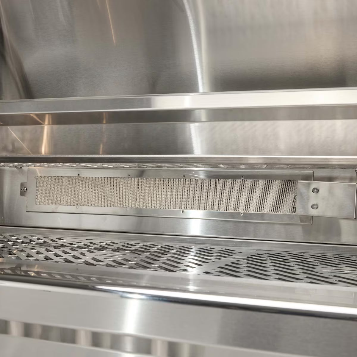 Interior of an open Coyote stainless steel grill showing the rear infrared burner with its rectangular mesh screen mounted at the back of the firebox, above the cooking grates
