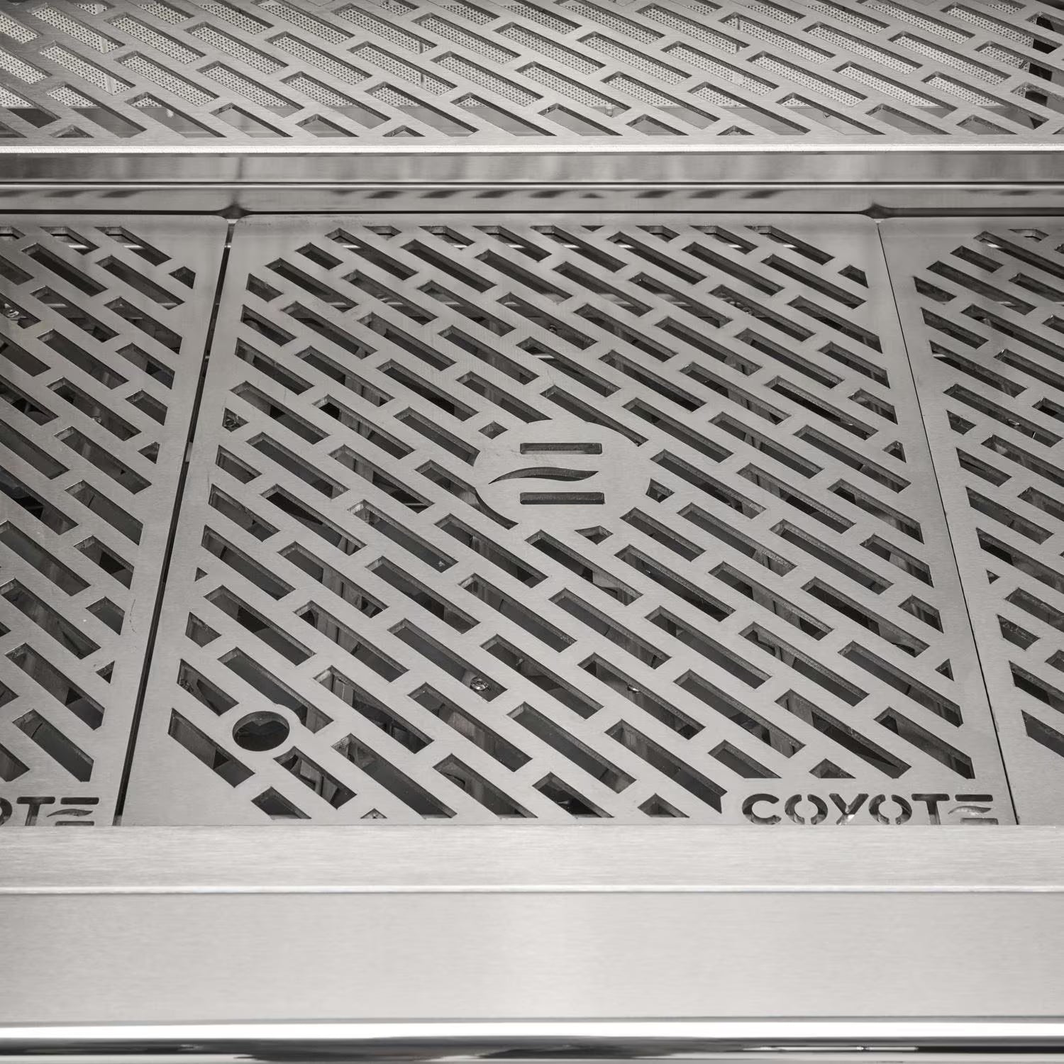 Top-down close-up of the Coyote-branded stainless steel cooking grates with the embossed Coyote logo, and the warming rack visible above