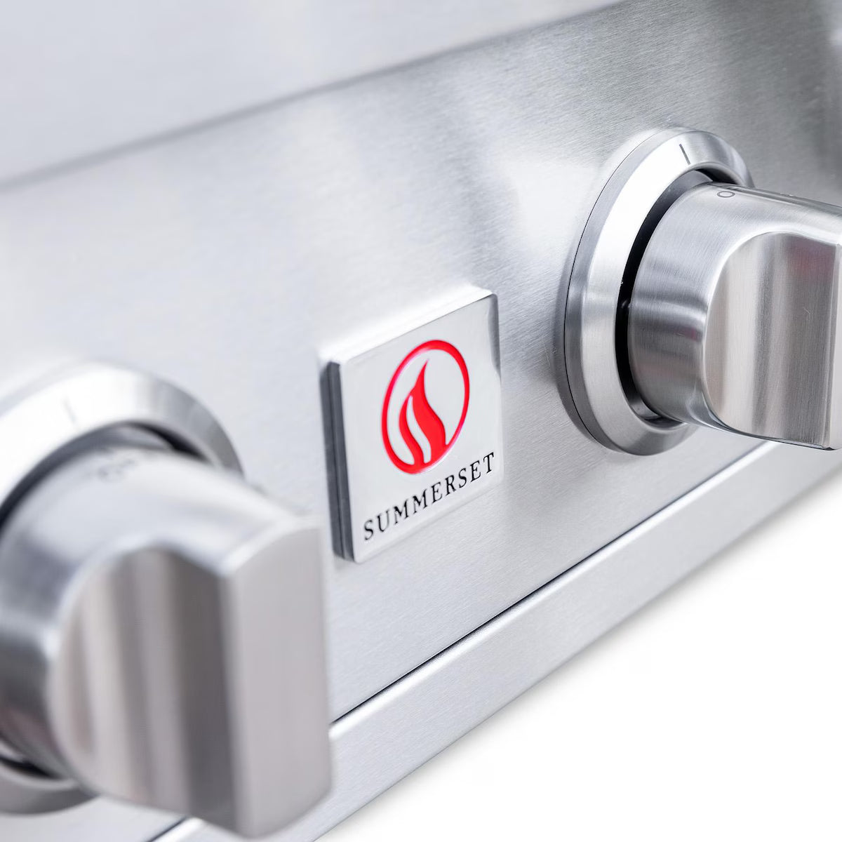 Close-up of the Summerset flame logo badge on the control panel between two knobs of a built-in gas grill