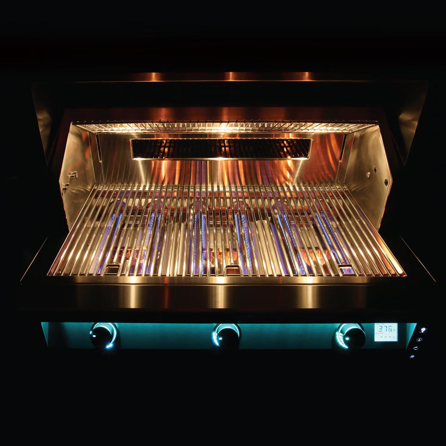 Front view of a built-in stainless steel grill with the lid open, showing the glowing lit interior, cooking grates, warming rack and a row of teal-blue backlit control knobs with a digital temperature display, on a black background