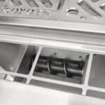 A close-up feature image looking down into a pellet grill cooking chamber showing the stainless steel firepot and auger pellet-delivery mechanism below the grates