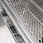 A close-up feature image looking into a pellet grill at an angle, showing the tiered stainless steel cooking grates above the auger pellet-feed area
