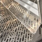A close-up feature thumbnail of the perforated stainless steel warming rack mounted inside the upper section of a built-in gas grill, viewed at an angle