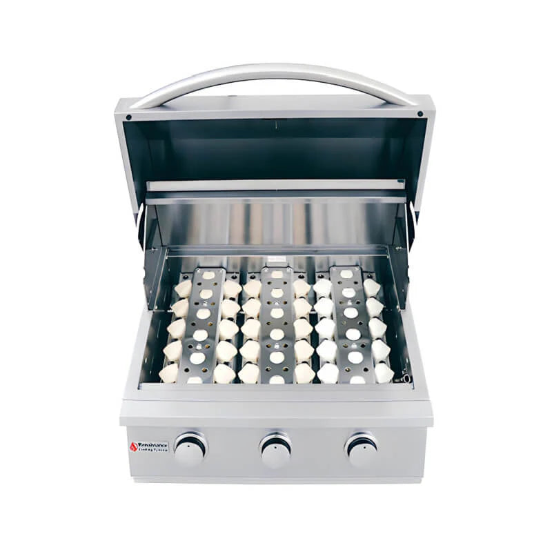 Angled view of an RCS Premier 26-inch three-burner built-in stainless steel gas grill with the lid open and grates removed, showing the white ceramic briquette trays seated over the burners, three control knobs and the Renaissance Cooking Systems logo, on a white background