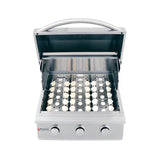 Angled view of an RCS Premier 26-inch three-burner built-in stainless steel gas grill with the lid open and grates removed, showing the white ceramic briquette trays seated over the burners, three control knobs and the Renaissance Cooking Systems logo, on a white background