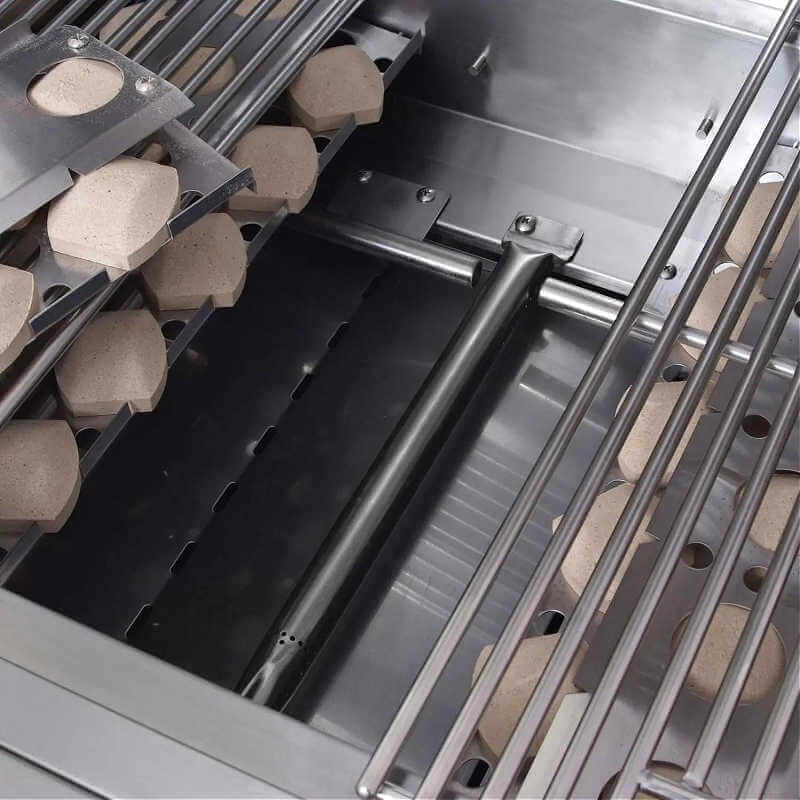 Close-up inside an RCS Premier grill firebox showing a tubular stainless steel burner running along the floor, flanked by ceramic briquettes in their trays beneath the cooking grates