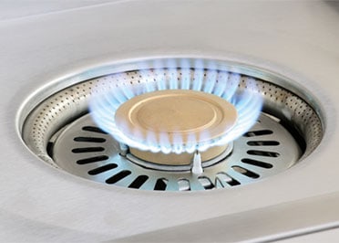 Alfresco 24-inch Versa Power cooker with the independent center burner lit under the brass cap, AIPGVP