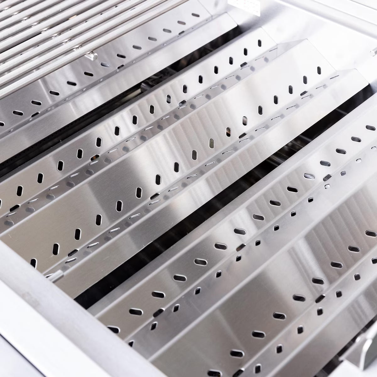 Close-up of a grill's stainless steel vented heat tents and flame tamers inside the firebox