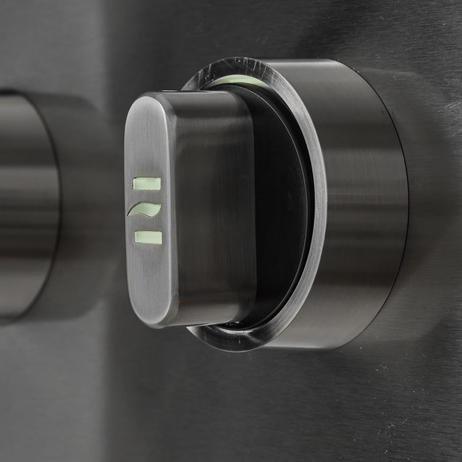 Close-up of a stainless steel grill control knob with illuminated green position markings, on a brushed metal control panel