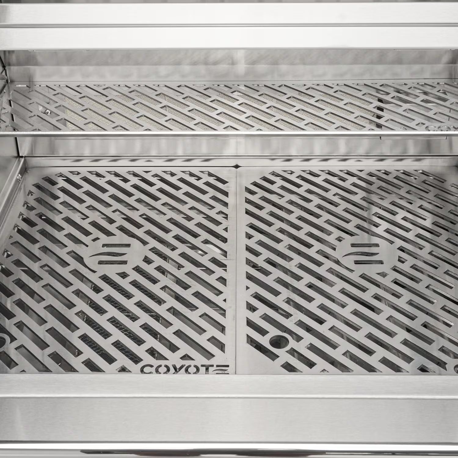 Interior front view of an open Coyote grill showing the Coyote-branded stainless steel cooking grates and the warming rack above
