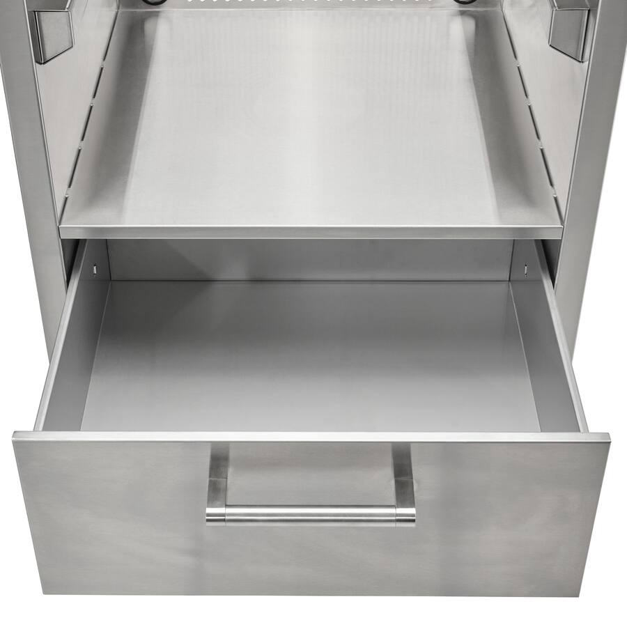 A close-up of the stainless steel built-in charcoal grill with its bottom storage drawer pulled fully open, showing the empty drawer interior and the tubular bar handle, against a white background
