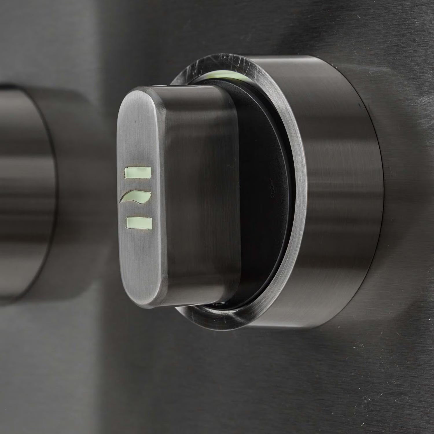 Close-up of a stainless steel grill control knob with illuminated green position markings, on a brushed metal control panel