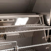 Interior of an open American Outdoor Grill showing stainless steel cooking grates, warming rack, halogen interior light, and rotisserie rod