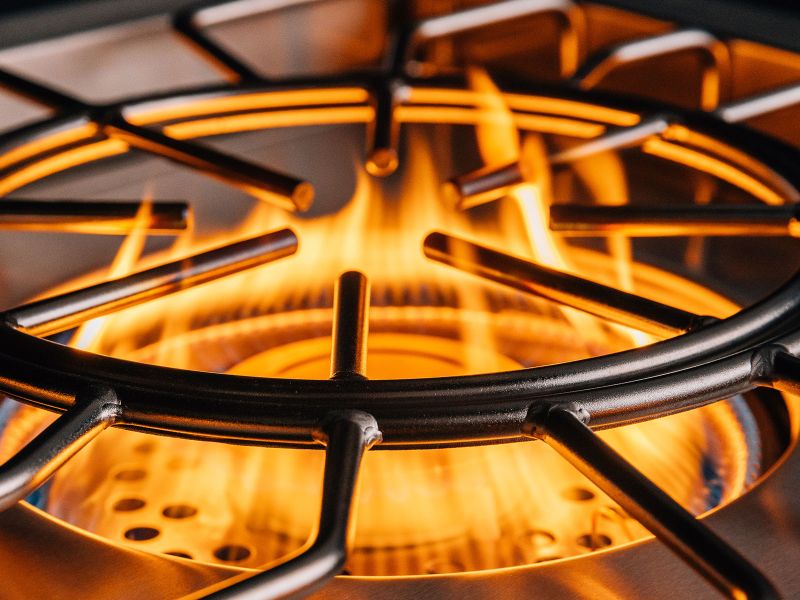 Close-up of a power burner's round cast iron grate with high orange flames beneath