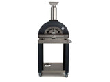 A black dome-top wood-fired outdoor pizza oven shown front-on, with the front face showing air vents and a temperature gauge, a stainless steel chimney, and a black cart stand with an open lower shelf and caster wheels, against a white background
