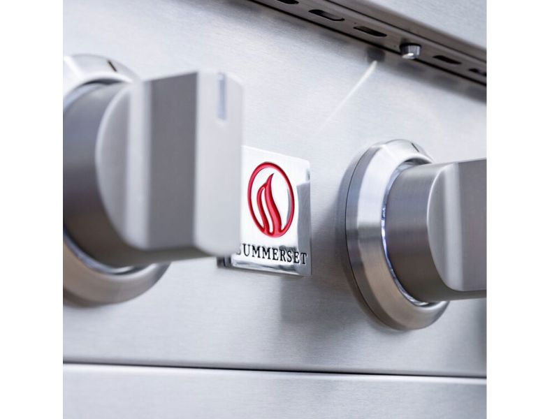 Summerset flame logo badge on the stainless steel control panel between knobs of a Sizzler Pro built-in gas grill