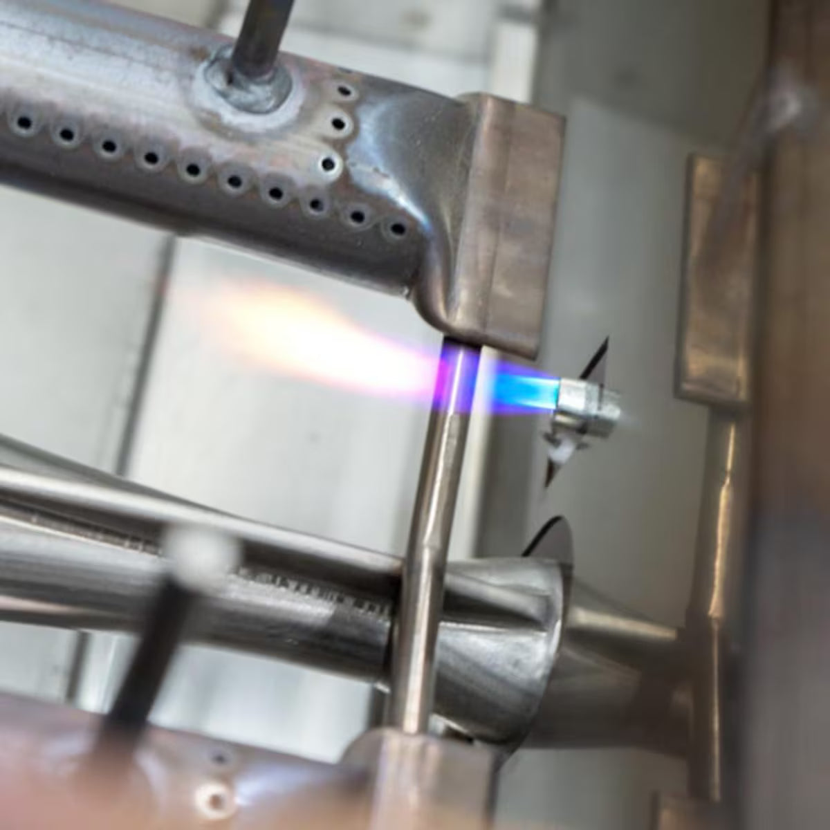 Close-up of a stainless steel grill burner igniting with a blue flame from the electronic igniter