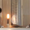 Close-up of a stainless steel grill burner ignition, showing the spark electrode lighting a small flame beside a perforated tube burner