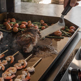 Steak, shrimp skewers, potatoes, and green beans cooking on a Blackstone electric drop-in griddle with a spatula