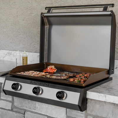 Blackstone 30-inch electric drop-in griddle with open lid cooking shrimp, lobster, and sausage on a marble outdoor counter