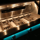 Angled interior view of an open Alfresco stainless steel grill lit by its interior lights, showing the tube burners and warming rack, with control knobs glowing teal-blue on the front panel