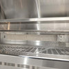 Interior of an open Coyote stainless steel grill showing the rear infrared burner with its rectangular mesh screen mounted at the back of the firebox, above the cooking grates