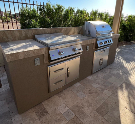 Travertine outdoor kitchen island with a stainless steel built-in gas grill and flat-top griddle on a stone patio