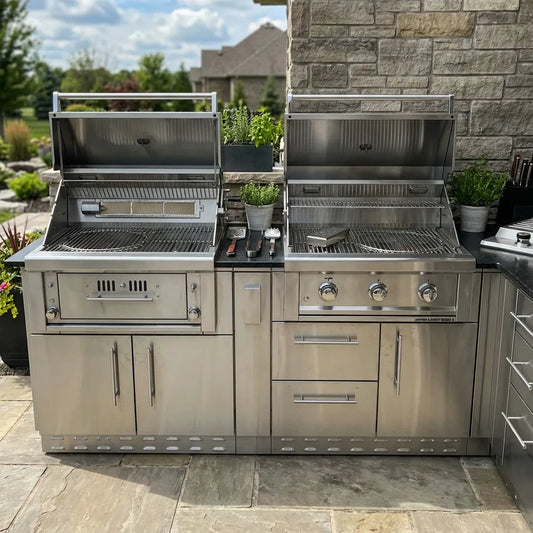Stainless steel built-in outdoor kitchen with two gas grills, storage drawers, and cabinets on a stone patio