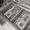 Interior of an open Coyote grill firebox showing the Coyote-branded stainless steel heat diffuser plates seated over the burner tray, with the warming rack above