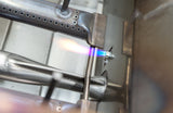 Close-up of AOG's Flame Thrower burner igniting on the grill's gas manifold, a product feature shot