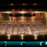 Interior of a lit built-in stainless steel grill with the lid open, showing blue gas flames beneath the cooking grates, a warming rack above, and three teal-blue backlit control knobs along the bottom