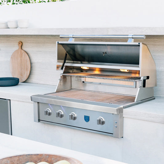 Stainless steel built-in gas grill with open lid and lit burners in a modern outdoor kitchen