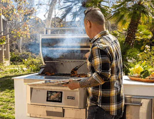 Man grilling food on a Coyote built-in gas grill in a backyard outdoor kitchen